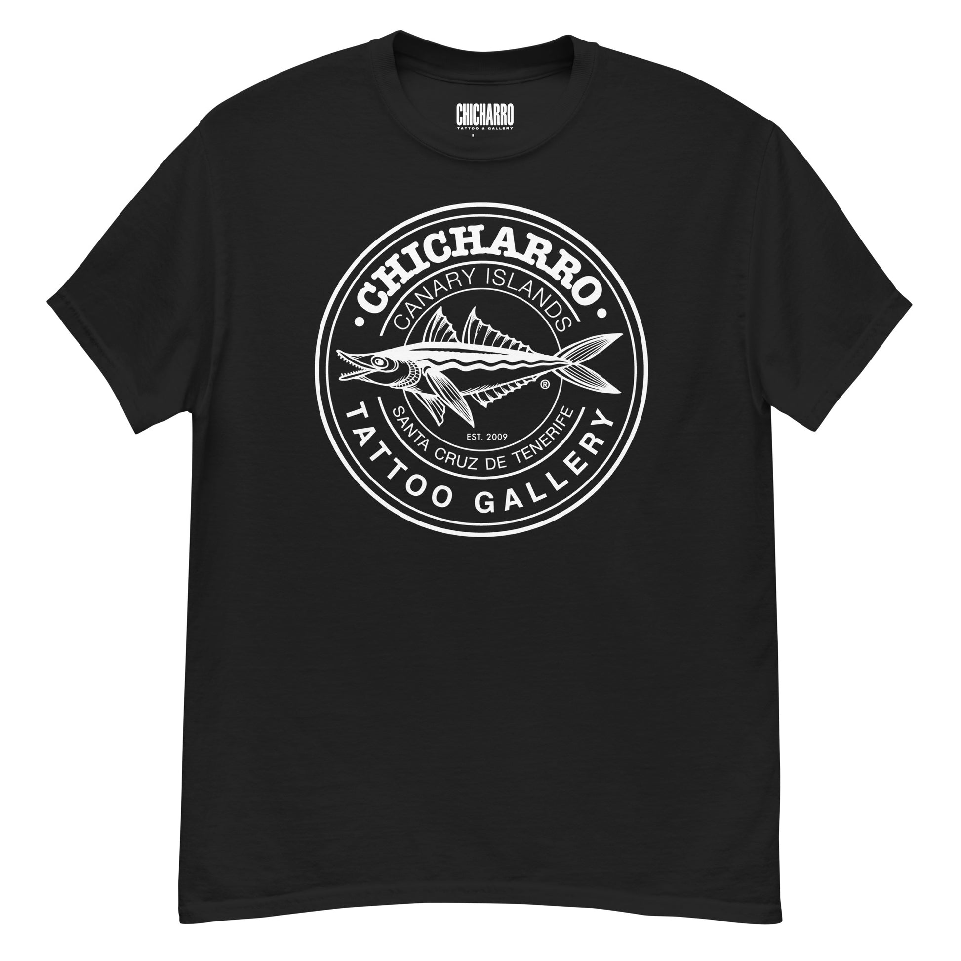 Camiseta negra, con un logotipo blanco en el centro. El logotipo representa a un chicharro dibujado de lado con la forma abierta. El chicharro está rodeado por un círculo, en el que aparecen las palabras CHICHARRO, TATTO GALLERY, CANARY ISLANDS y SANTA CRUZ DE TENERIFE.